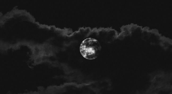 A full white moon in a dark sky with clouds