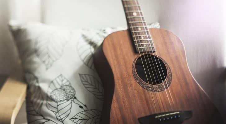 A brown guitar leans against a pillow