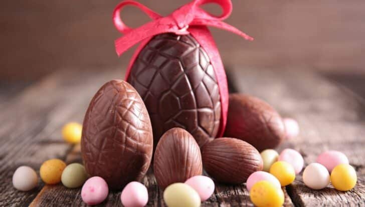 A variety of chocolate Easter eggs, including a larger one tied with a red ribbon, surrounded by small pastel-colored chocolate eggs