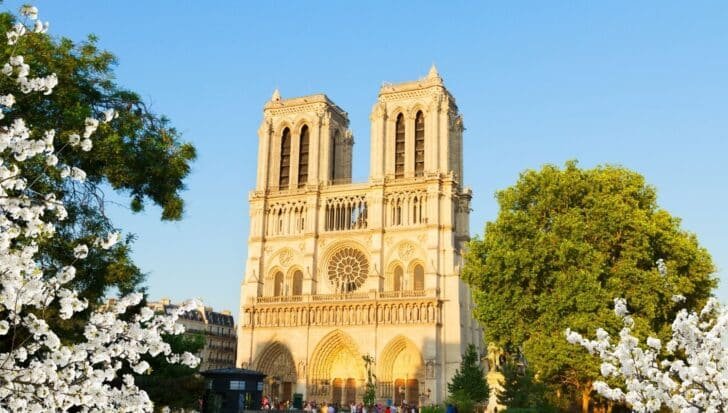Notre Dame Cathedral's facade with its twin towers, surrounded by blooming trees, highlighting its architectural beauty