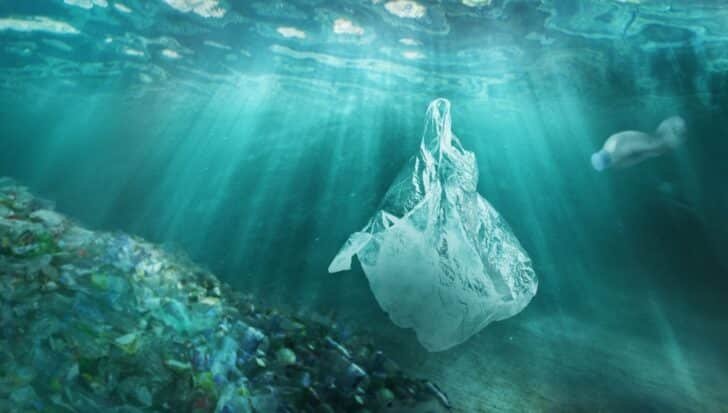 Underwater scene with a floating plastic bag, a plastic bottle, and a pile of plastic debris, illustrating ocean pollution