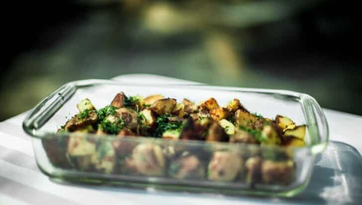 A pyrex glass dish containing roasted potatoes with herbs