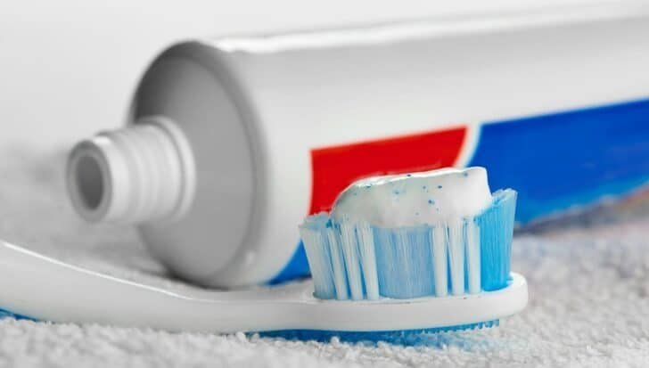A toothbrush with toothpaste on the bristles next to an open toothpaste tube