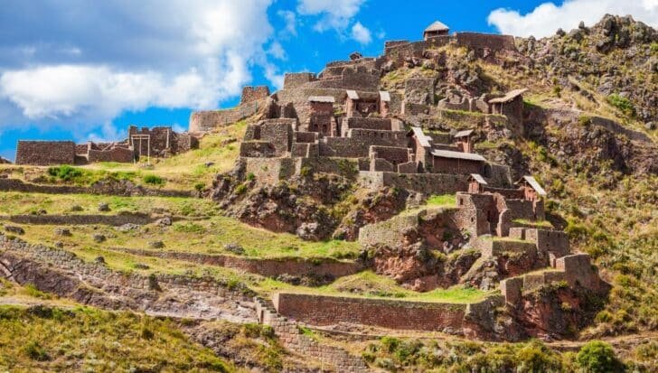 Ancient Inca ruins situated on a hillside, showcasing intricate stonework and terraced architecture under a bright blue sky with clouds