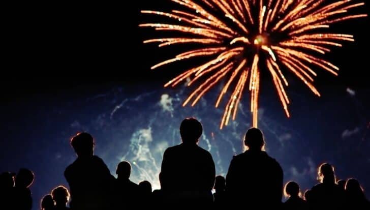 Silhouetted people watching a large firework display against a night sky