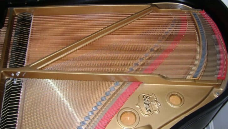 Close-up of the inside of a piano showing strings and structure labeled Sofmer, highlighting its dual nature as a stringed and percussion instrument