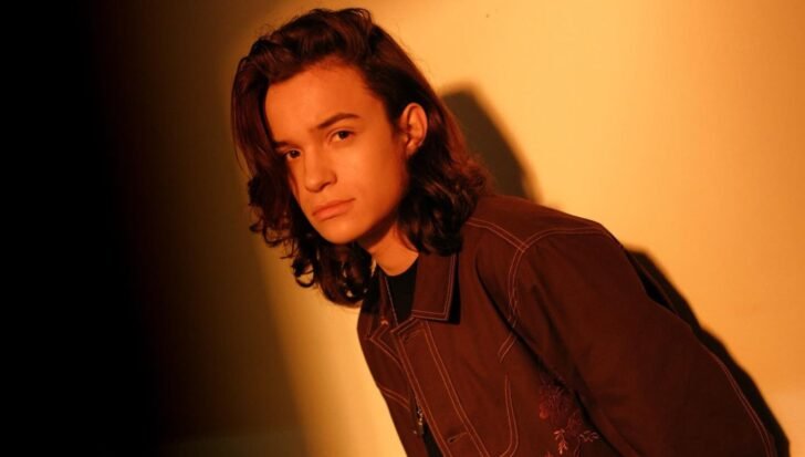 Nicolas Alves wearing a jacket, posed against a warm-colored background