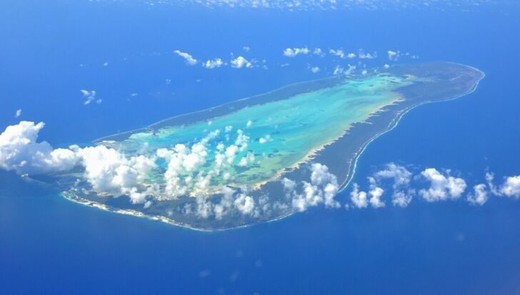 Aerial view of Aldabra Atoll surrounded by the Indian Ocean with visible coral reefs and clouds.